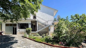 A two-story house with a stone-paved courtyard, a small garden with various plants, and a satellite dish on the roof. - Apartman Hida (Jadranovo)