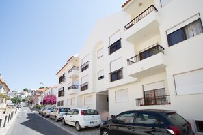 A row of white apartment buildings with balconies, parked cars, and a clear sky. - BeGuest Parede Beach Apartment - Cascais (Parede)