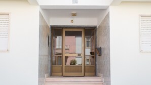 Una entrada de edificio con puertas dobles, una planta pequeña en maceta y una escalera que sube.
