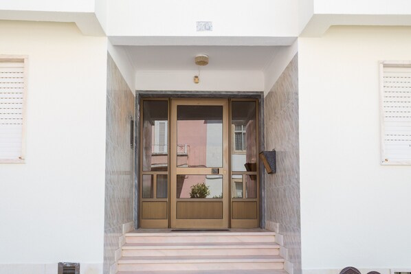 A building entrance with a double door, a small potted plant, and a staircase leading up. - BeGuest Parede Beach Apartment - Cascais (Parede)