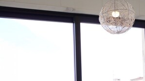 Un comedor con una mesa preparada para dos personas, una ventana con vistas a edificios y una lámpara colgante.