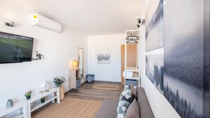 A modern living room with a flat-screen TV, a sofa, a coffee table, and a wall-mounted air conditioner.