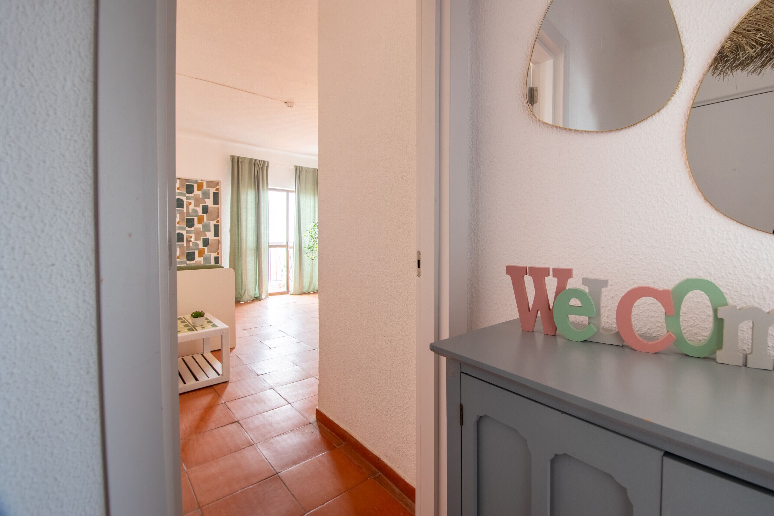 A hallway with a 'Welcome' sign, a mirror, and a small table with a plant.