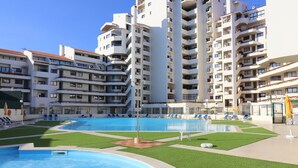 Ein Swimmingpool, umgeben von grünem Kunstrasen, mit mehreren Balkonen und weißen Gebäuden im Hintergrund.