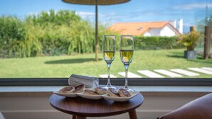 A table with plates of food and two glasses of wine, a menu, and a view of a house and garden through a window.