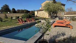 A swimming pool with lounge chairs, a stone building, and a small tree in the foreground. - Mas provençal, garden, swimming pool and playground for children (Montboucher-sur-Jabron)