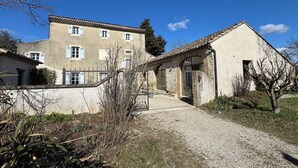 A two-story building with a tiled roof, a gravel driveway, and a small garden area with shrubs and a tree. - Mas provençal, garden, swimming pool and playground for children (Montboucher-sur-Jabron)
