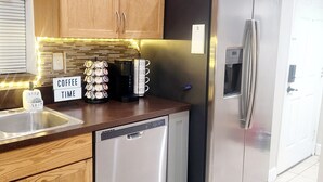 A modern kitchen with wooden cabinets, stainless steel appliances, a coffee station, and a dishwasher. - Charming 2-bedroom, 2.5 bath townhome in Gainesville - WiFi, AC, parking & more! (Gainesville)