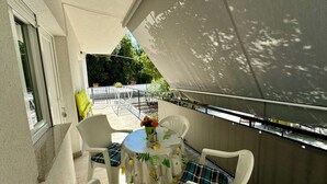 A balcony with a table and chairs, a white chair with a plaid cushion, and a potted plant. - Apartment Kristina 2 (Jadranovo)