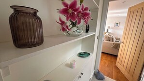 Ein weißes Schränkchen mit einer Vase voller pinkfarbener Blumen, einer kleinen Schale und einer Kerze.