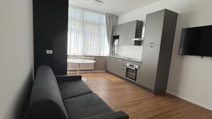 En moderne stue med sofa, spisebord, et køkkenområde og et fjernsyn.