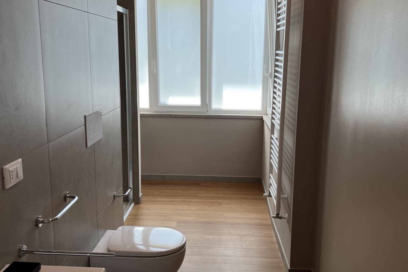 Ein schmales Badezimmer mit Toilette, Haltegriff und Fenster.