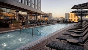 A rooftop pool area with lounge chairs, a bar, and a view of the cityscape.