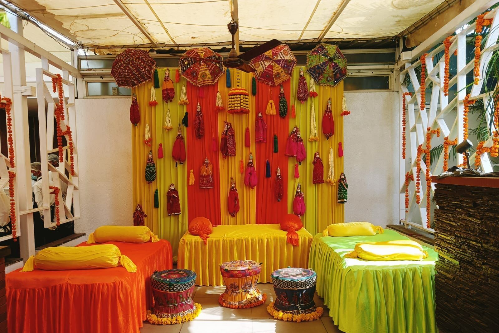 A room with colorful drapes and hanging decorations, multiple beds with vibrant bedding, and traditional Indian musical instruments.
