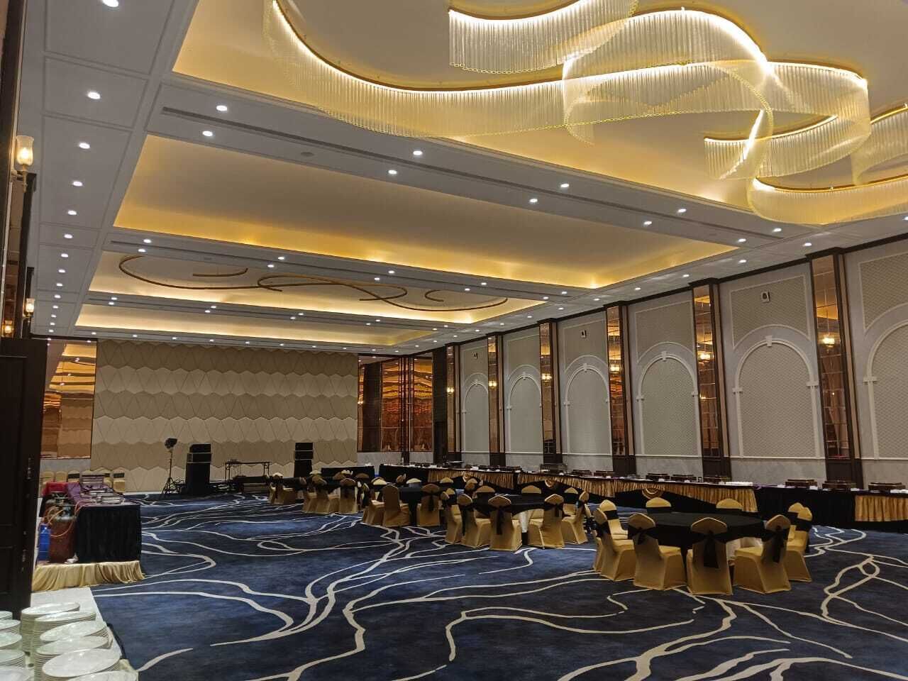 Un amplio salón de conferencias con filas de mesas y sillas, un escenario y una alfombra estampada.