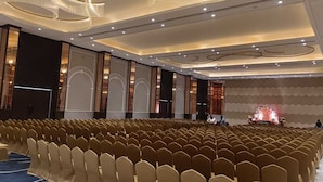 A conference room with rows of chairs, a stage with a decorative backdrop, and a modern ceiling design. - Enrise By Sayaji Bhopal (Bhopal)