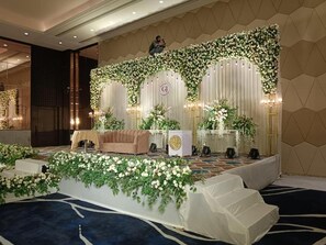 A stage with a floral backdrop, a sofa, and a podium. - Enrise By Sayaji Bhopal (Bhopal)