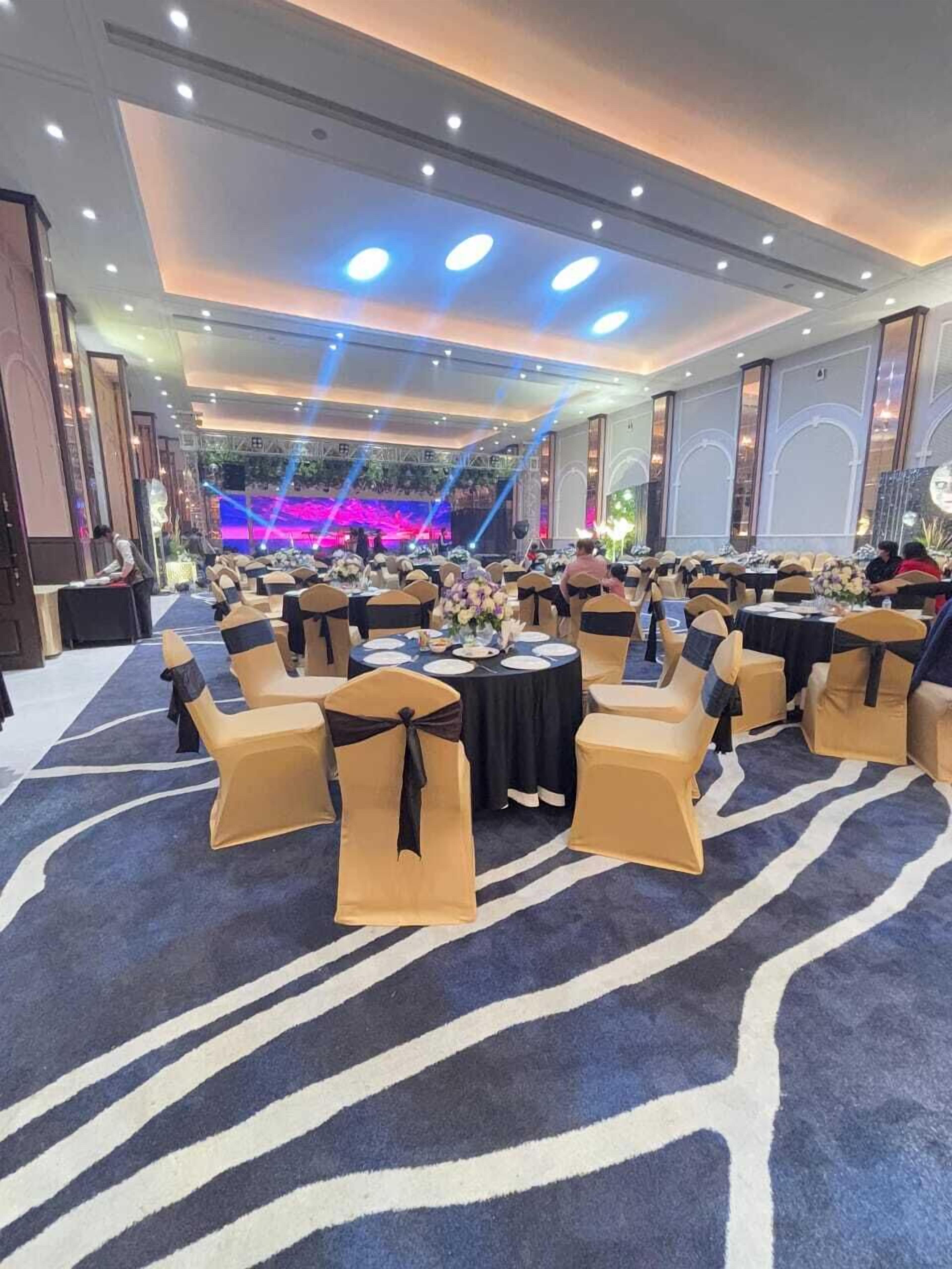 A banquet hall with round tables, chairs, and a stage with a blue light backdrop.