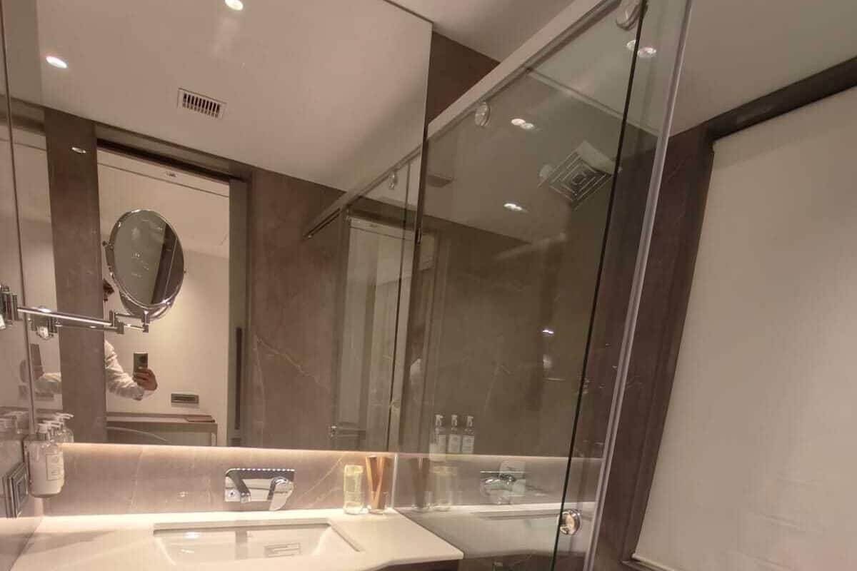 A modern bathroom with a glass shower enclosure, a marble sink, and a mirror with a round frame.