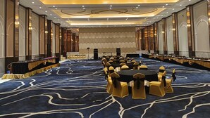 A large conference room with round tables and chairs, a stage with a podium, and a patterned carpet. - Enrise By Sayaji Bhopal (Bhopal)