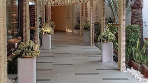 A corridor with a tiled floor, white pillars, and hanging garlands with red flowers. - Enrise By Sayaji Bhopal (Bhopal)