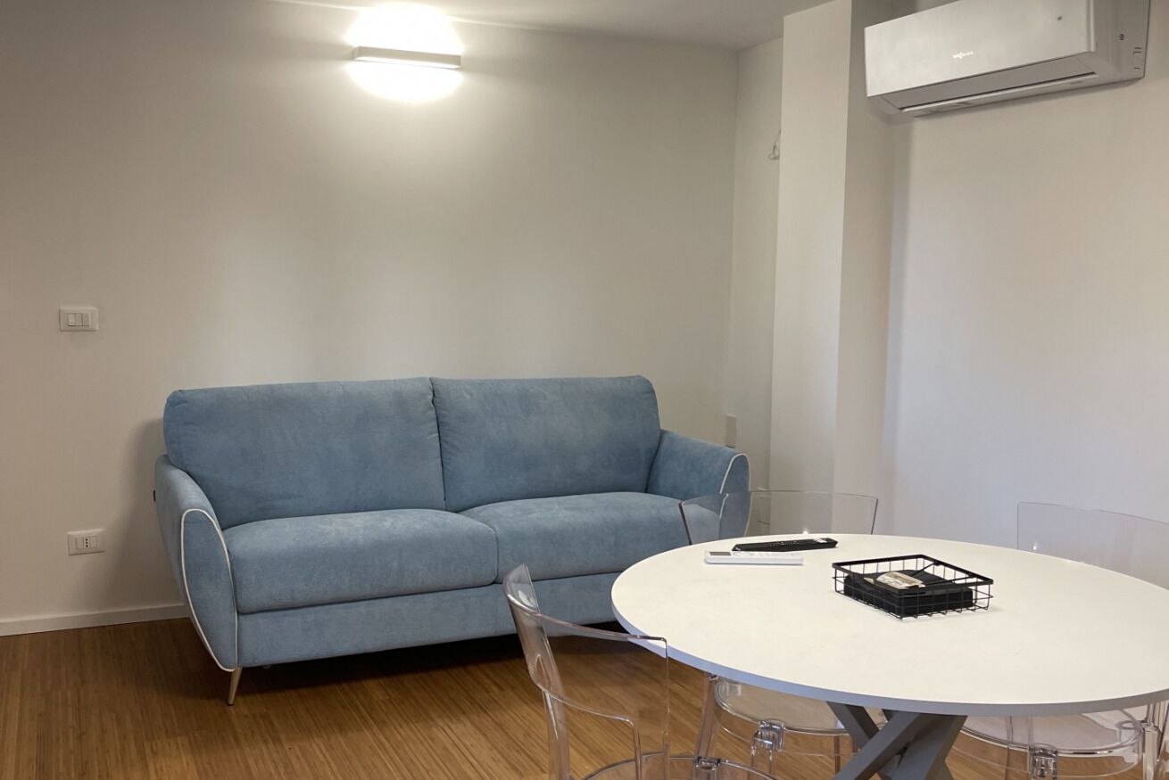 Une pièce avec un canapé bleu clair, une table ronde blanche et un panier de rangement noir posé sur la table.