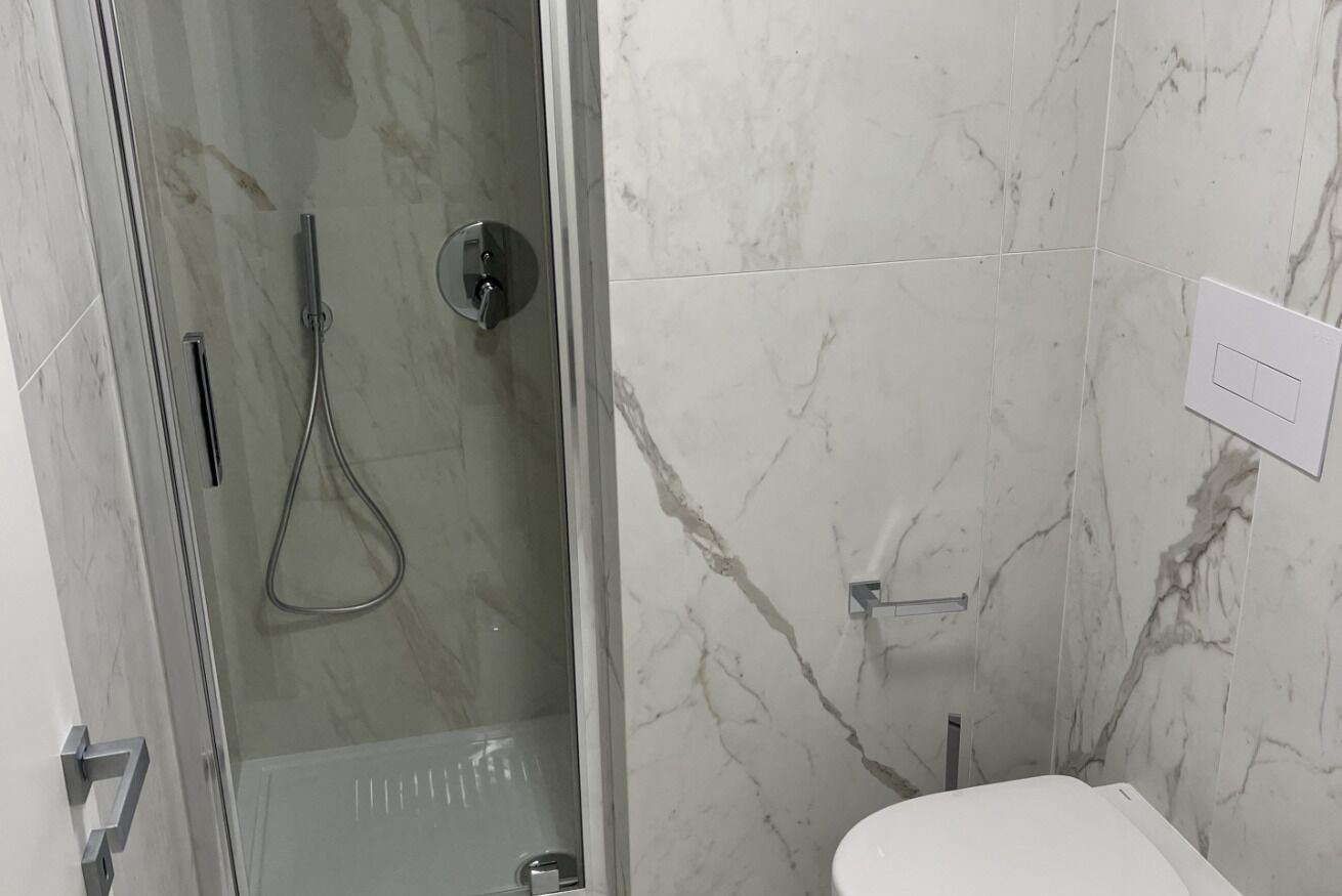 Een badkamer met een douche in een glazen cabine, een wit toilet en marmeren wanden.
