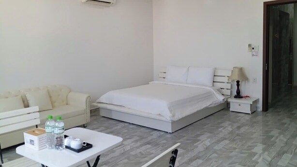 Ein modernes Hotelzimmer mit Bett, einer Couch, einem kleinen Tisch mit Pflegeprodukten und einer Klimaanlage.