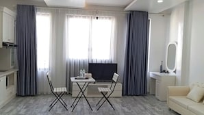 Ein modernes Wohnzimmer mit Fernseher, einer Couch, einem Esstisch mit Stühlen und einer kleinen Küchenzeile.