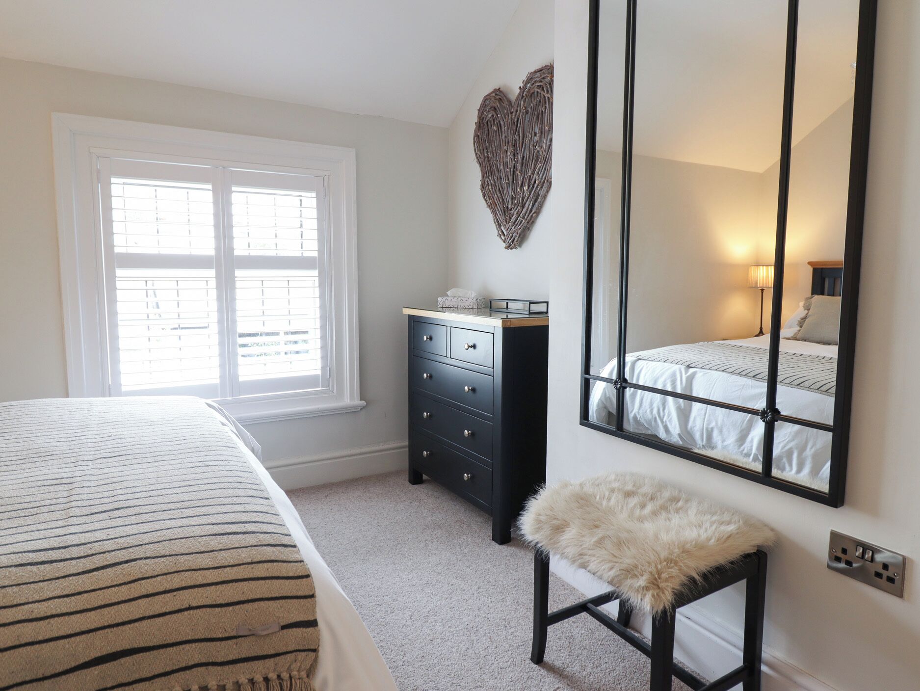 A bedroom with a bed, a dresser, a mirror, and a window with blinds.