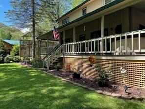 A two-story building with a covered porch, a staircase, and a flag. - Copper Lady Cottage - Creekside 3 BR, 2BA, Hot Tub, Firepit (Maggie Valley)