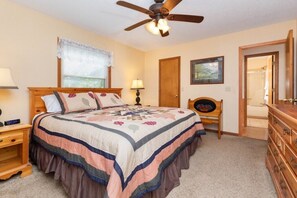 A bedroom with a bed, a ceiling fan, a nightstand, a dresser, and a door leading to another room. - Copper Lady Cottage - Creekside 3 BR, 2BA, Hot Tub, Firepit (Maggie Valley)