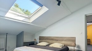 A bedroom with a skylight, a bed with a floral bedspread, a wooden headboard, and a nightstand with a lamp. - Gîte le Foch, rated 3 ***, large gîte in the center of Albi, ideal for groups/families, (Albi)