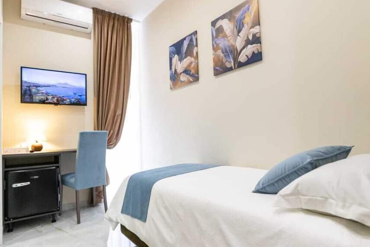 Habitació d'hotel amb llit, escriptori, cadira, televisió i obres d'art a la paret.
