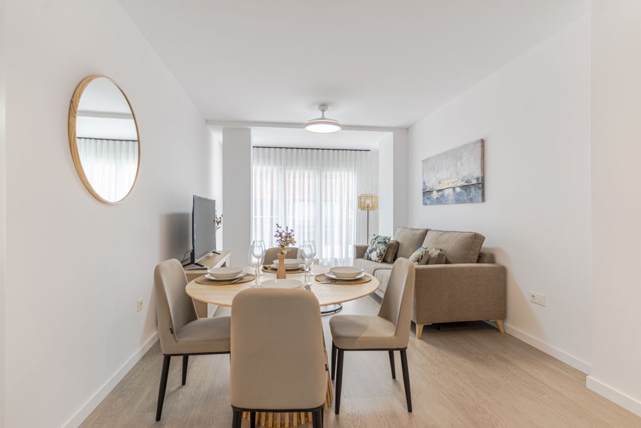 Un salon moderne avec une table à manger ronde, des chaises de couleur beige, un canapé et un grand miroir accroché au mur.