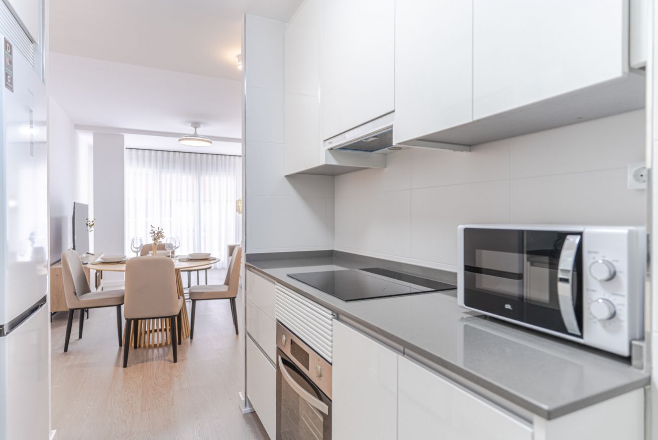 Een moderne keuken met witte kasten, een inbouwmagnetron en een eethoek met een tafel en stoelen.
