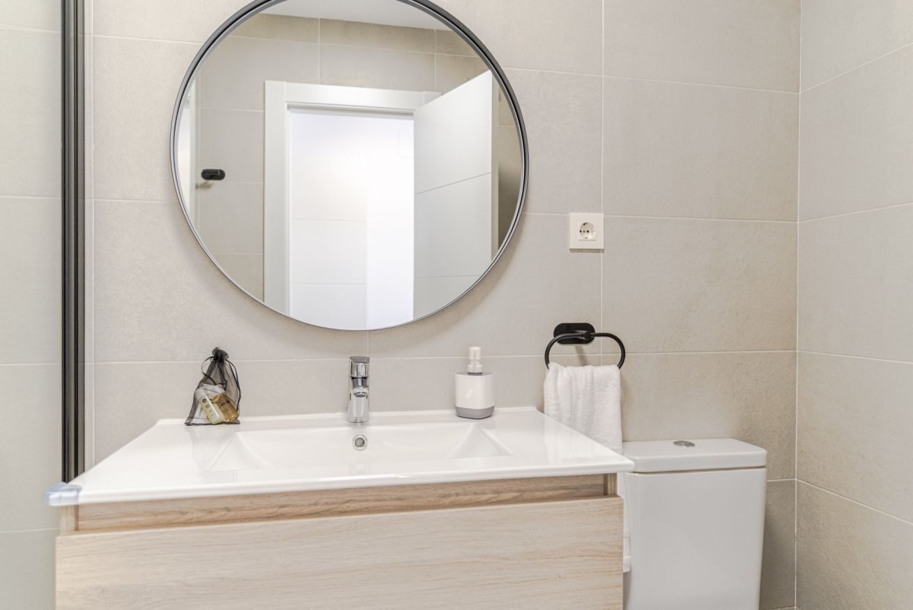 Une salle de bain avec un miroir rond, un lavabo blanc et des toilettes.