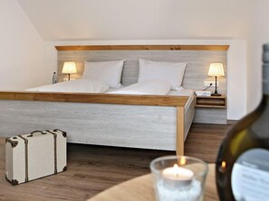 A bedroom with a wooden bed frame, two bedside tables with lamps, a suitcase, and a candle on a table. - Weingut Hillabrand (Willanzheim)