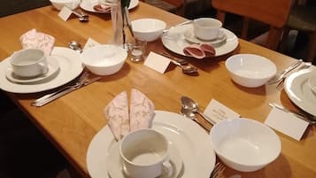 A dining table set with white plates, bowls, cups, and cutlery, accompanied by a vase with flowers and a small glass.