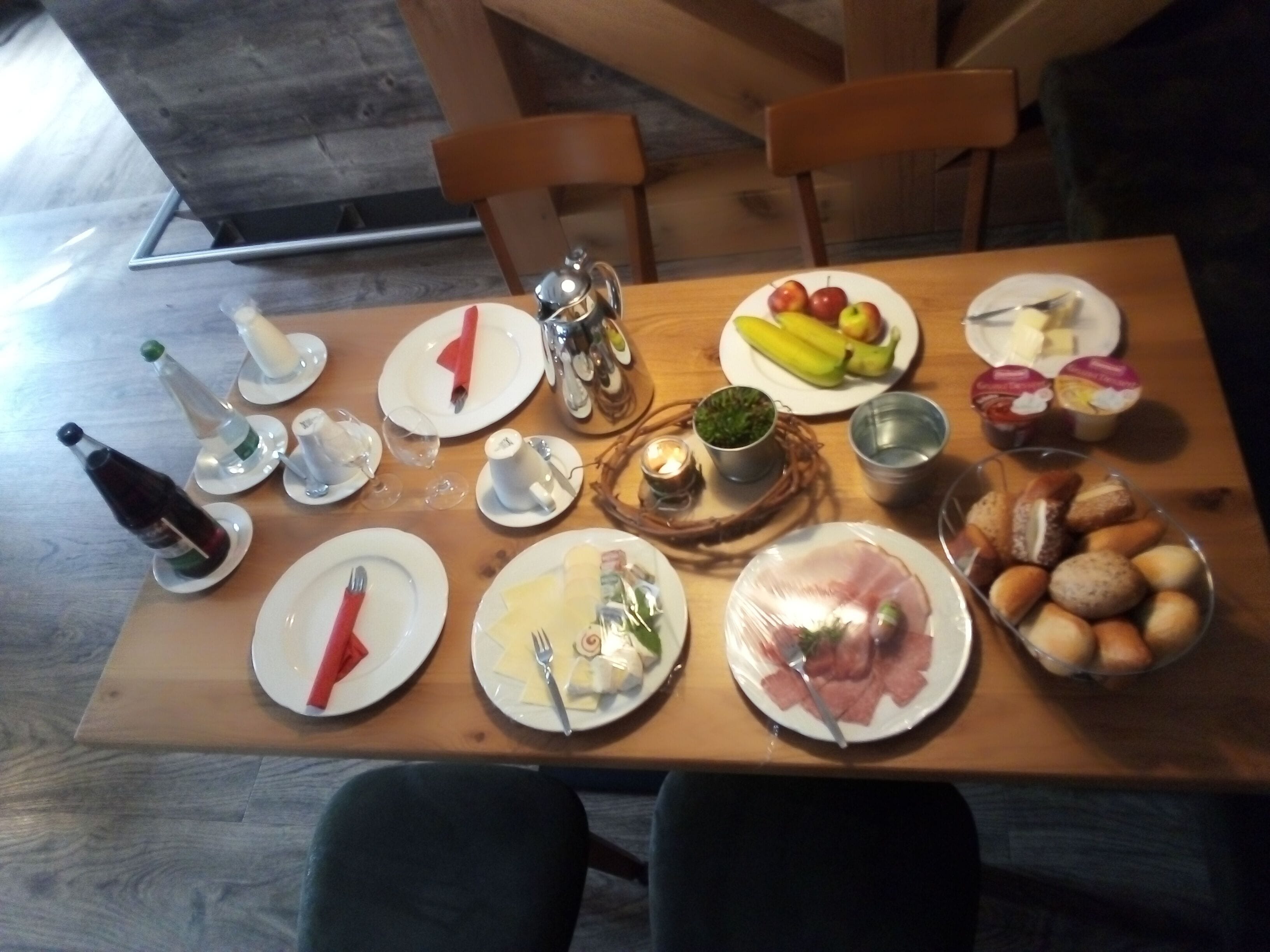 A wooden dining table set with plates, cutlery, and various food items, including fruits and bread.
