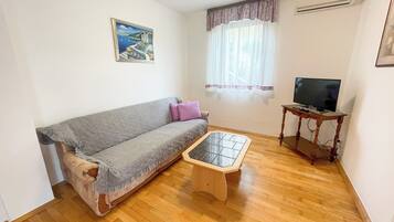 Una sala de estar con sofá, una mesa de centro, un televisor sobre un soporte de madera y una ventana con cortinas.