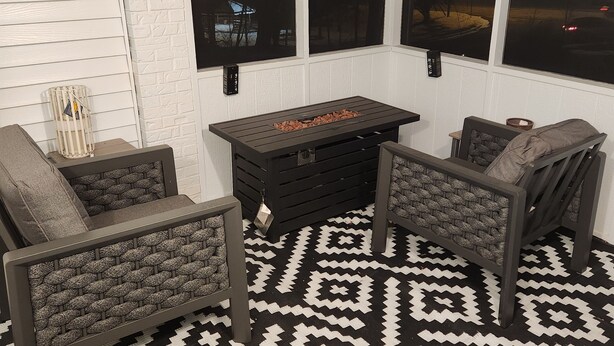 Un espace extérieur accueillant, avec deux chaises et une table, un tapis à motifs et une vue sur le ciel nocturne grâce à de grandes fenêtres.