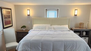 Une chambre bien rangée, avec un lit, des tables de chevet, une chaise, une lampe fixée au mur et un luminaire au plafond.