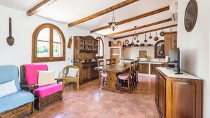 A spacious living room with a large window, a dining area with wooden furniture, and a kitchen with hanging utensils.