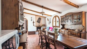 A rustic kitchen with wooden beams, a fireplace, and a dining area with a wooden table and chairs.