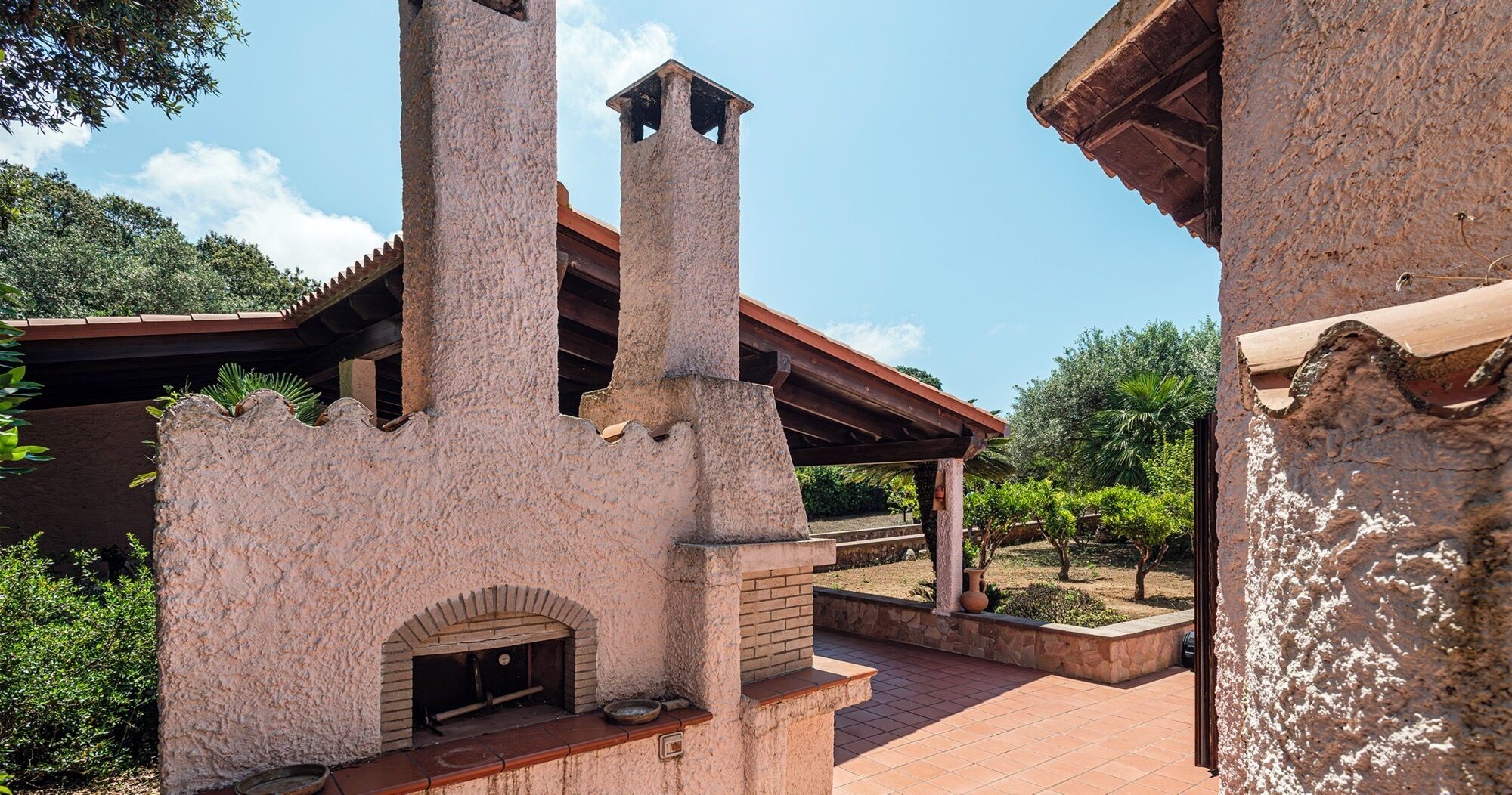 Un bâtiment en pierre doté d’une cheminée, d’un four en briques et d’un patio couvert.