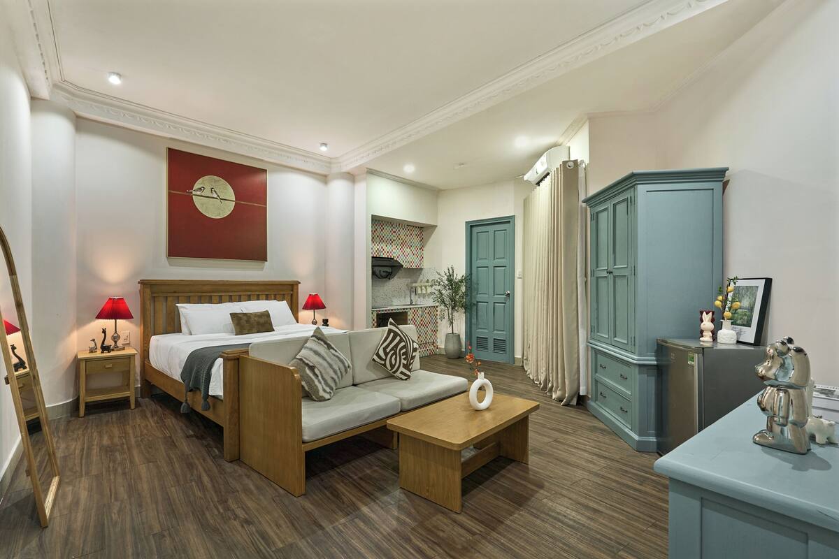 A modern hotel room with a wooden bed, a sofa, a coffee table, a desk, and a wardrobe.
