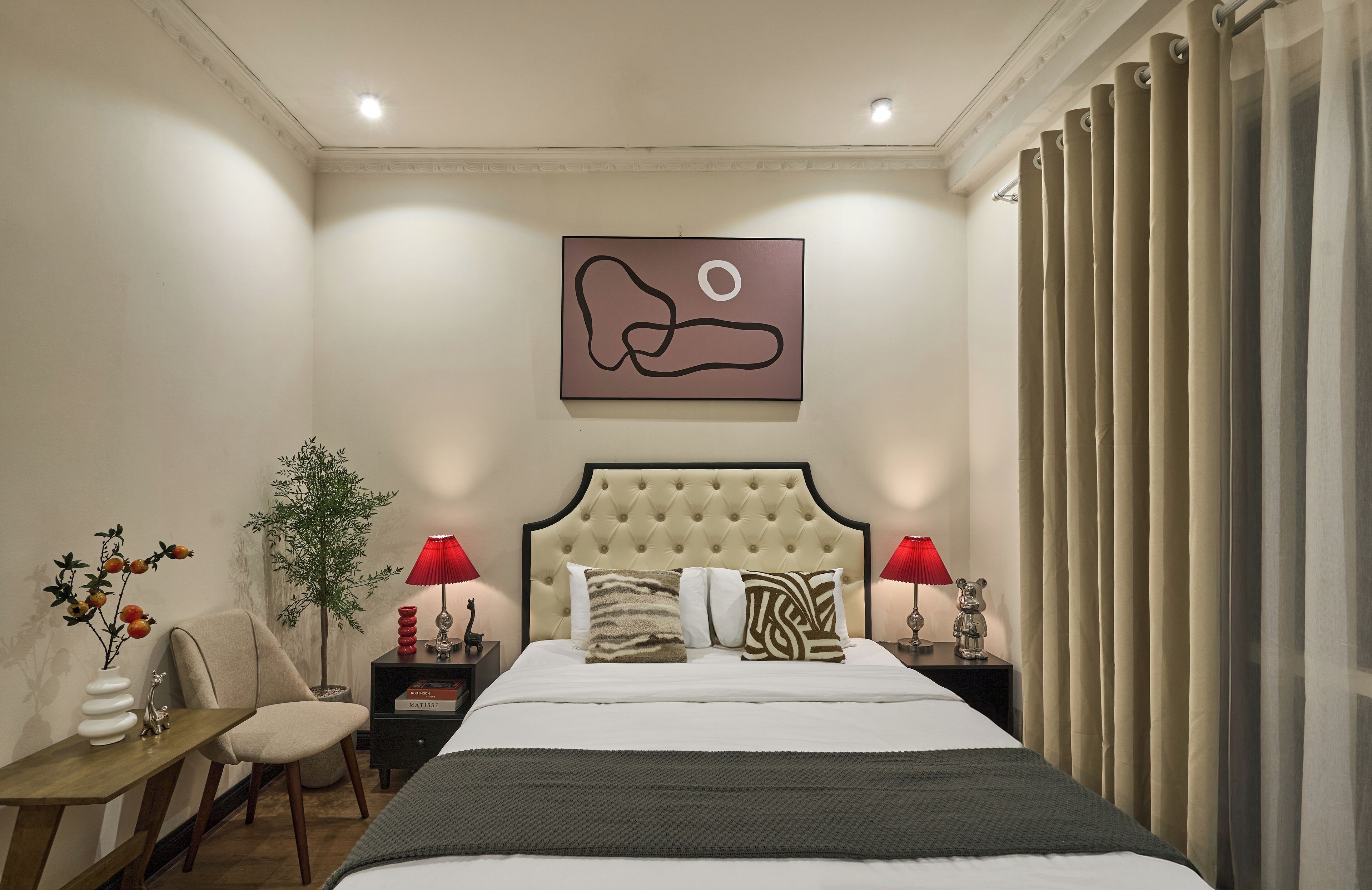 Habitación de hotel con cama, dos mesitas de noche, una silla, una planta en maceta y una obra de arte en la pared.