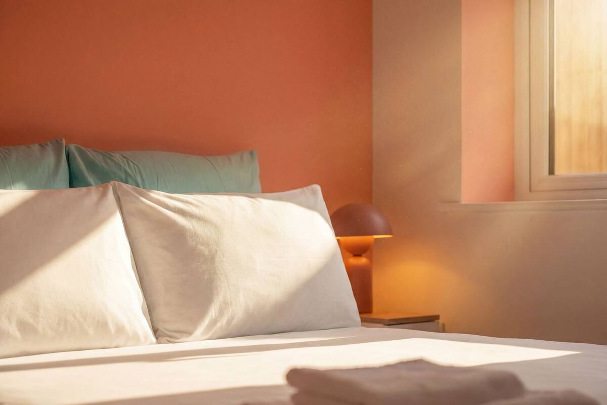 A neatly made bed with white linens and a folded towel, a teal pillow, and a lamp on a bedside table.