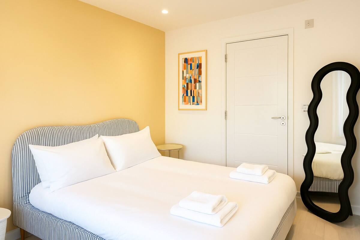 A hotel room with a bed, a bedside table, a mirror, and a door.